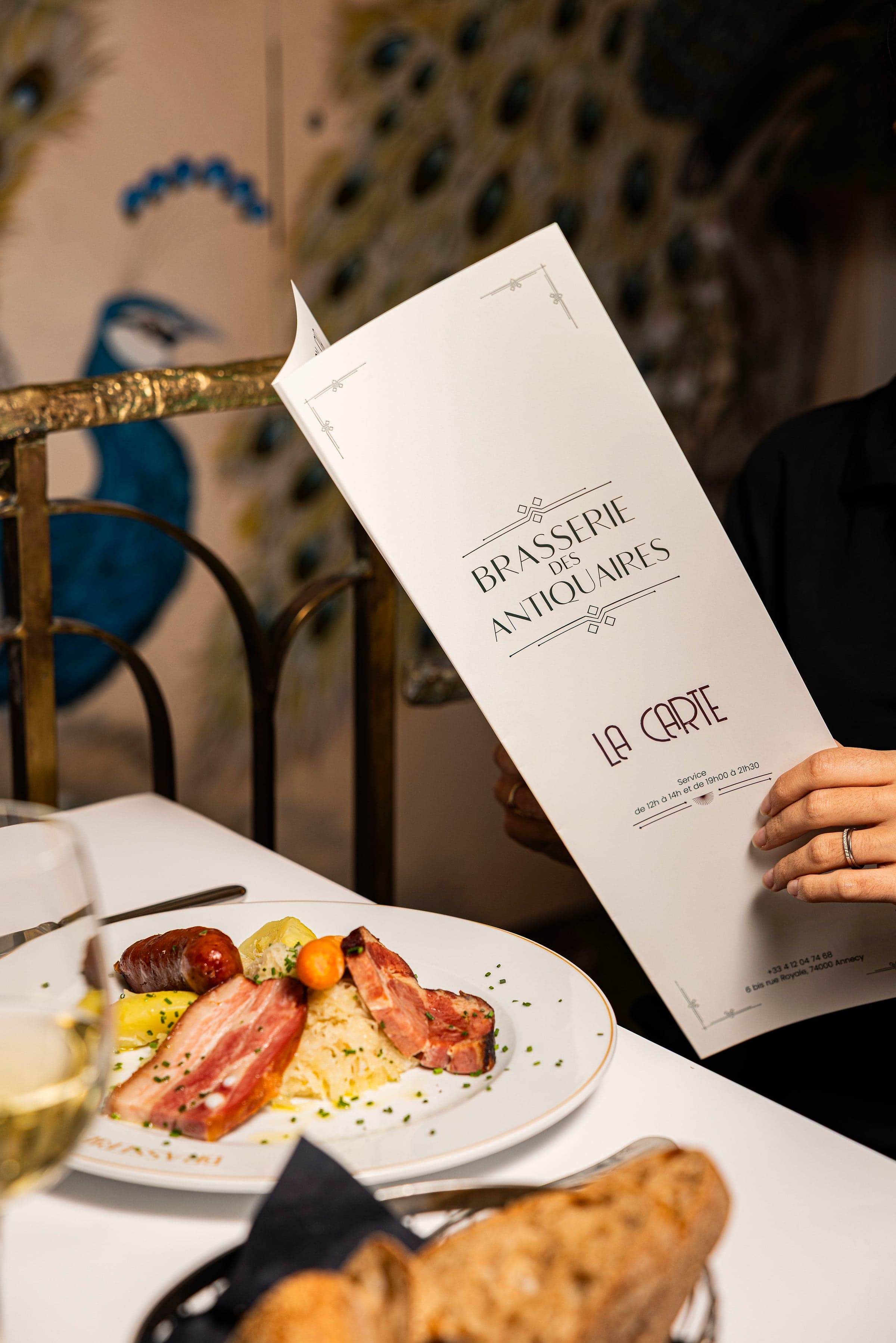 La carte de la maison tenue à table, devant la fresque au paon de la salle